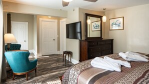 Une chambre d’hôtel comprenant un lit, un ventilateur de plafond, une télévision, une commode et une chaise.