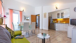 Un soggiorno moderno con un divano verde, un'area pranzo con tavolo in vetro e una cucina con mobili bianchi e forno integrato.