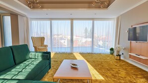 Una sala de estar moderna con un sofá verde, una mesa de centro de madera, un sillón estampado y un ventanal con cortinas ligeras.