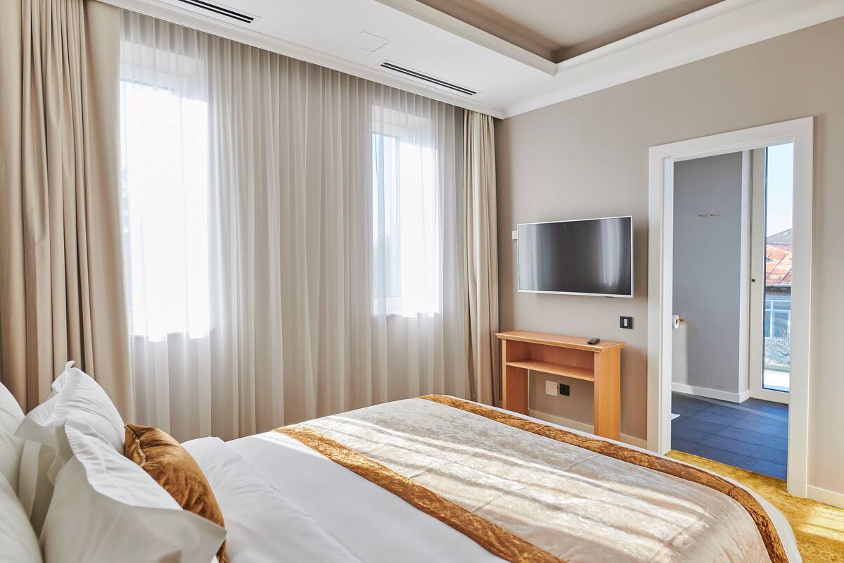 Una camera d'albergo con un letto grande, una TV a parete e un'uscita che dà su un balcone.