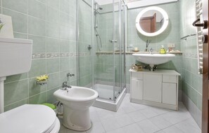 Ett badrum med en dusch som är avskärmad med glasväggar, ett handfat, en toalett och en bidé.