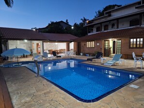 Ein Schwimmbad mit Liegestühlen und Sonnenschirmen, umgeben von Steinplatten und einem Ziegelgebäude mit einem Ziegeldach.