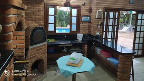 A rustic kitchen with a brick oven, a window overlooking a pool, and a small table with a cup. - Holiday Home in Atibaia  (Atibaia)