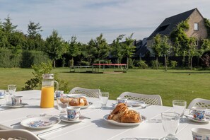 An outdoor dining area with a table set for breakfast, including croissants and a pitcher of orange juice. - Villa De Ruiter / Waasmunster (Waasmunster)