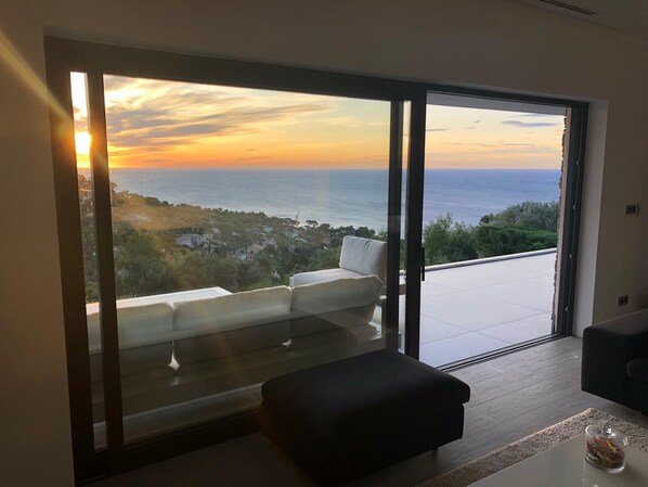 Un soggiorno moderno con un'ampia vetrata che si apre su un balcone con vista sulla costa.