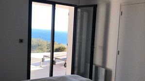 Une chambre à coucher avec un lit et une porte-fenêtre coulissante donnant sur un balcon avec vue sur la mer.