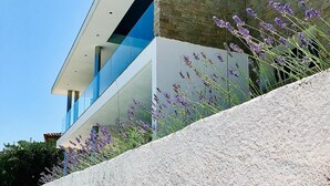 Un bâtiment moderne doté d’une façade en pierre et d’un balcon en verre donnant sur un espace paysager agrémenté de plantes de lavande.