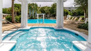 Zona de hidromasaje con piscina al fondo, rodeada de palmeras y sillones de descanso.