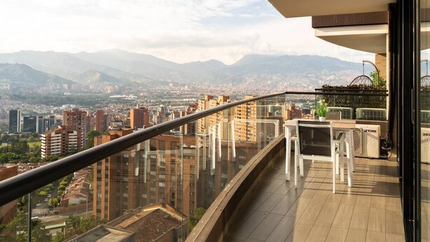 Ein Balkon mit Glasgeländer mit Blick auf eine Stadtlandschaft und Berge.