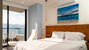 Ein modernes Hotelzimmer mit einem großen Bett, Blick auf die Berge und einem Gemälde des Ozeans an der Wand.