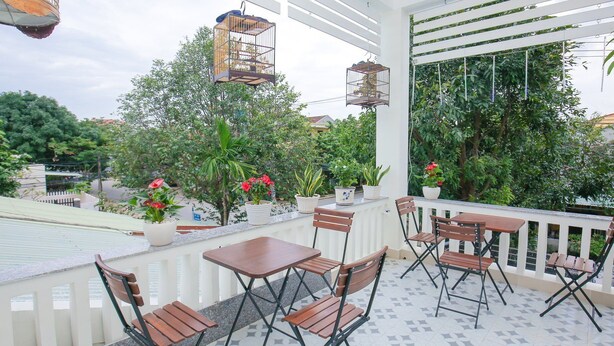 Un espace extérieur aménagé avec des tables et des chaises, entouré de plantes en pot et d’une rambarde.