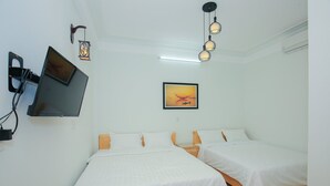 Une chambre dotée de deux lits simples, d’un téléviseur à écran plat fixé au mur, d’un tableau encadré et d’un luminaire suspendu.