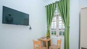 Une petite pièce avec un téléviseur fixé au mur, une table avec deux chaises et une fenêtre ornée de rideaux verts.