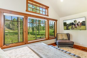 Un dormitorio con ventanas amplias, una cama, una silla y un cuadro de un campo de golf.