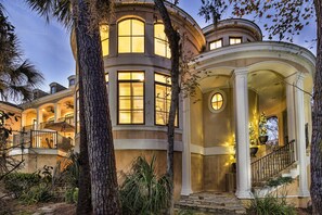 A grand house with multiple large windows, a covered porch, and a staircase leading to an upper level. - Luxury Retreat | Infinity Pool | Walk to Beach, Coligny, Dining & Shopping (Hilton Head Island)