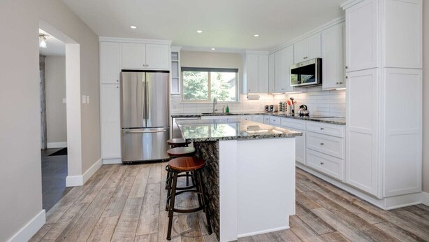 A modern kitchen with white cabinetry, a stainless steel refrigerator, a granite countertop, and a window providing natural light. - Gorgeous Vacation Chalet: Hot Tub, Wood Stove (Big Sky)