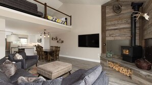 A spacious living area with a high ceiling, a fireplace, a dining area, and a kitchen. - Gorgeous Vacation Chalet: Hot Tub, Wood Stove (Big Sky)