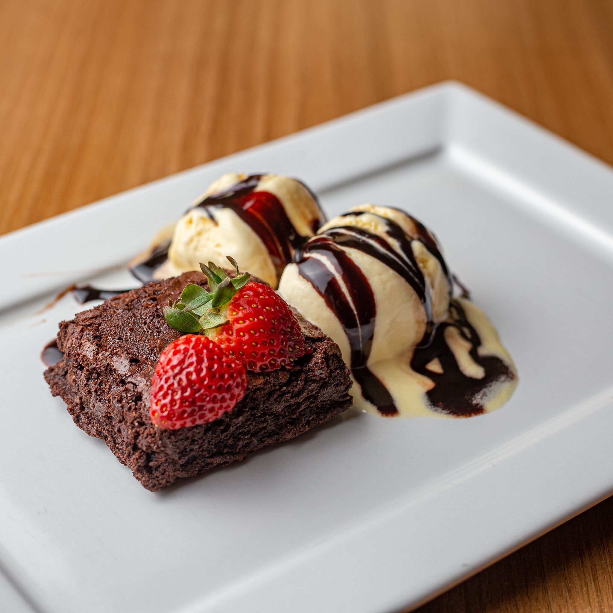 A dessert plate with a brownie, ice cream, and chocolate sauce.