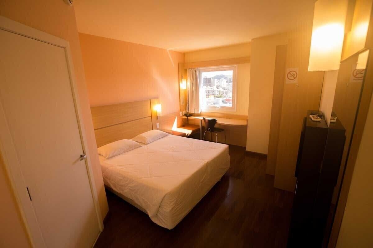 A hotel room with a bed, a desk, a chair, a window with a view, and a telephone.