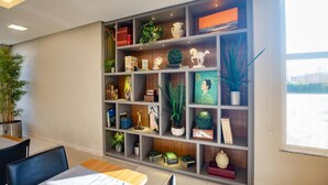 Una camera moderna con una libreria a muro piena di libri, oggetti decorativi e piante. È presente un'area pranzo con tavolo e sedie.