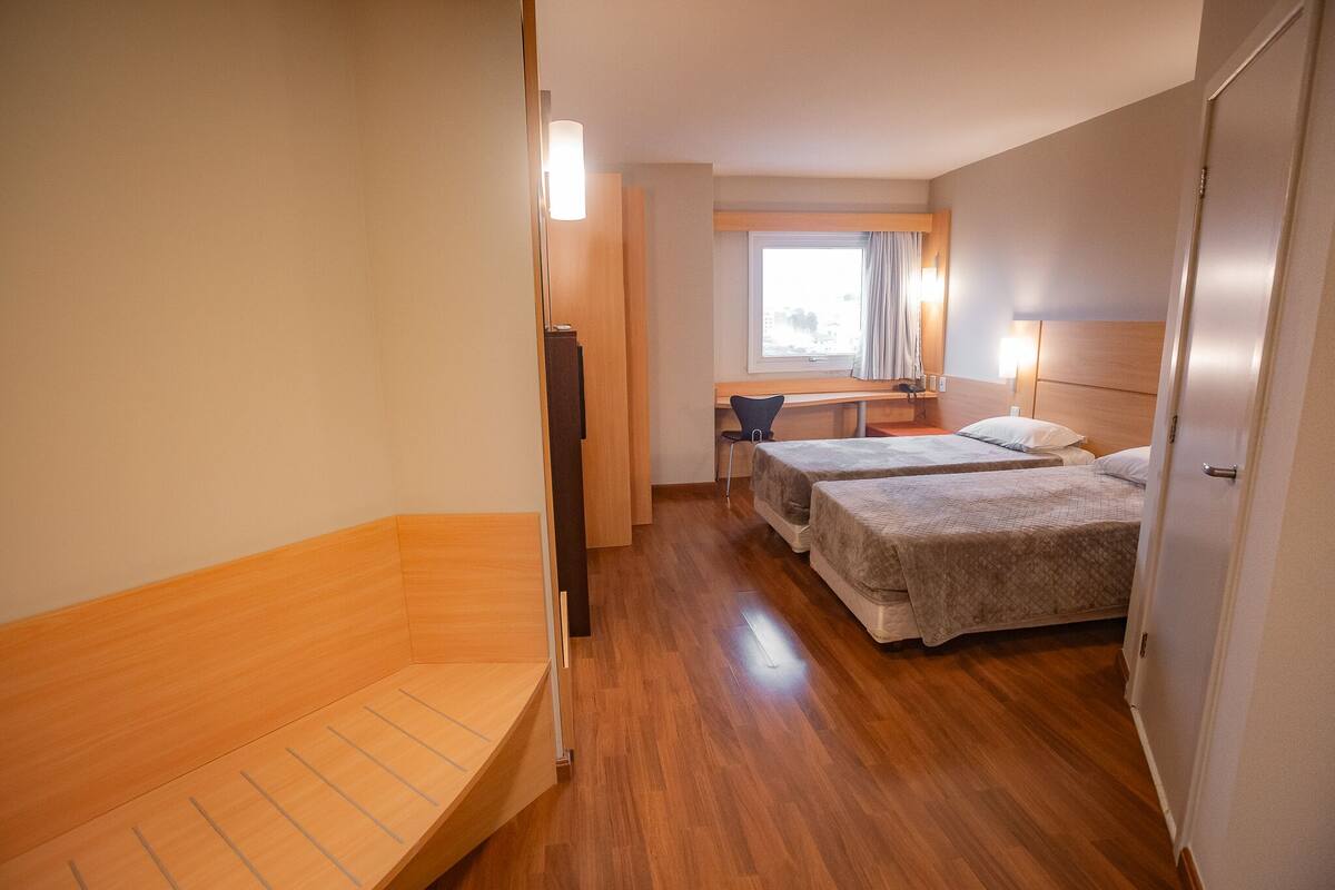 Habitación de hotel con dos camas, un escritorio, una silla y una ventana.