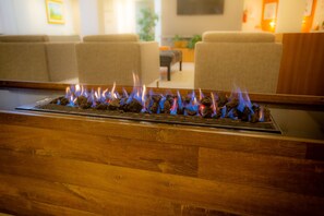 Una chimenea moderna con repisa de madera, rodeada de sofás color beige en una habitación bien iluminada.
