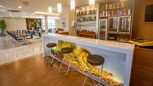 Zona bar moderna con bancone, sgabelli e una varietà di bottiglie e bicchieri sugli scaffali.