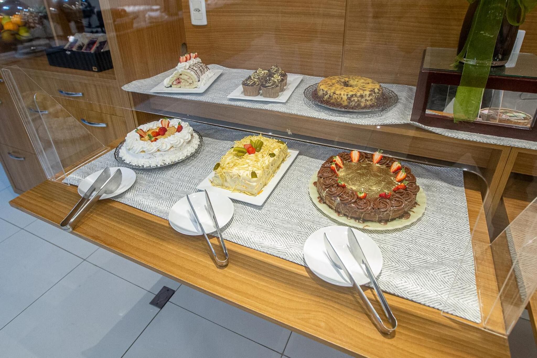 A display of various cakes on a counter with plates and cutlery.