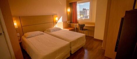 A hotel room with two beds, a desk, and a chair.