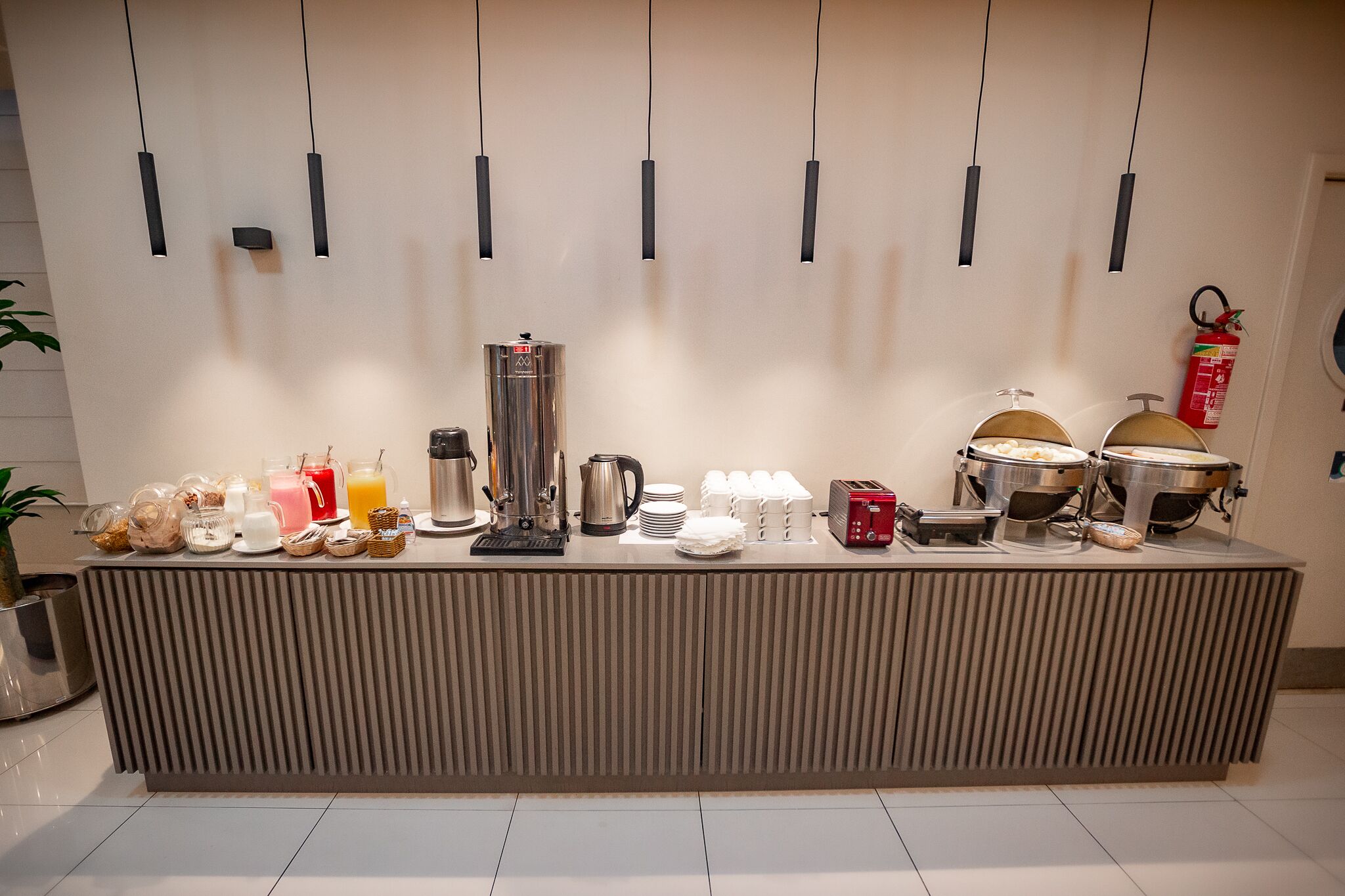 A buffet setup with various food and drink items, including a coffee maker, a kettle, and a toaster.