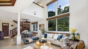 A spacious living room with a large window, a staircase, and a dining area. - 🏖️Peaceful | Concierge Included | Mauna Lani (Kamuela)