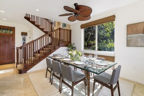 A dining area with a glass table, wooden chairs, and a ceiling fan. - 🏖️Peaceful | Concierge Included | Mauna Lani (Kamuela)