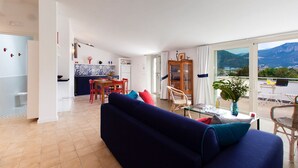 A modern living room with a sofa, dining area, and a view of mountains through large windows. - AMORE RENTALS - Casa Iommart with Private Terrace, Air Conditioning and Internet Wi-Fi (Sant´Agnello)