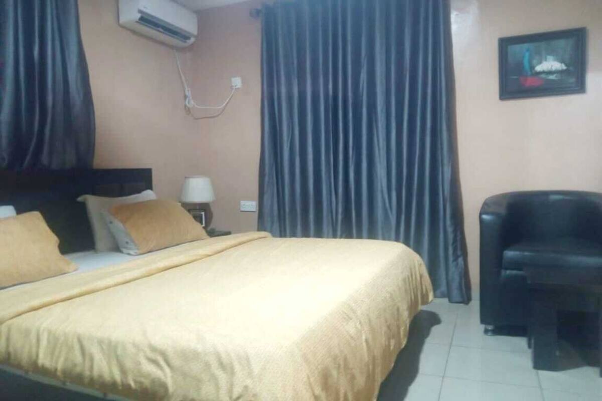 A hotel room with a bed, a chair, a desk, an air conditioner, and a wall-mounted TV.
