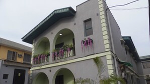 A two-story building with a balcony on the second floor, a green awning, and a potted plant in the foreground.
