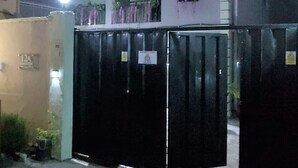 A gated building with a closed black gate, a white facade, and a balcony with plants.
