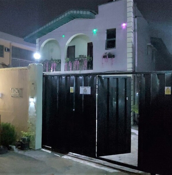 A gated building with a closed black gate, a white facade, and a balcony with plants.