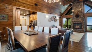 Un vaste espace de vie comprenant une grande table à manger en bois, des sièges confortables, une cheminée en pierre et une vue sur l’extérieur.