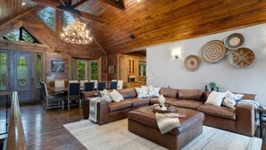 Un salon spacieux avec un grand canapé d’angle, un lustre et un coin repas comprenant une table et des chaises en bois.