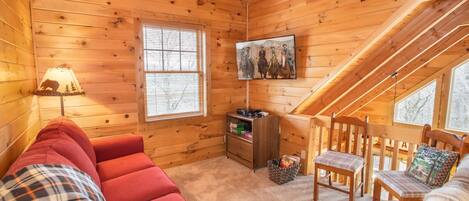 Ein gemütliches Blockhaus-Interieur mit einem roten Sofa, Holzwänden, einem kleinen Holztisch und einem Fenster mit Jalousien.