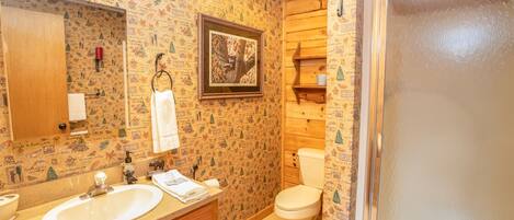 Un baño con tocador de madera, lavamanos, inodoro y zona de ducha.