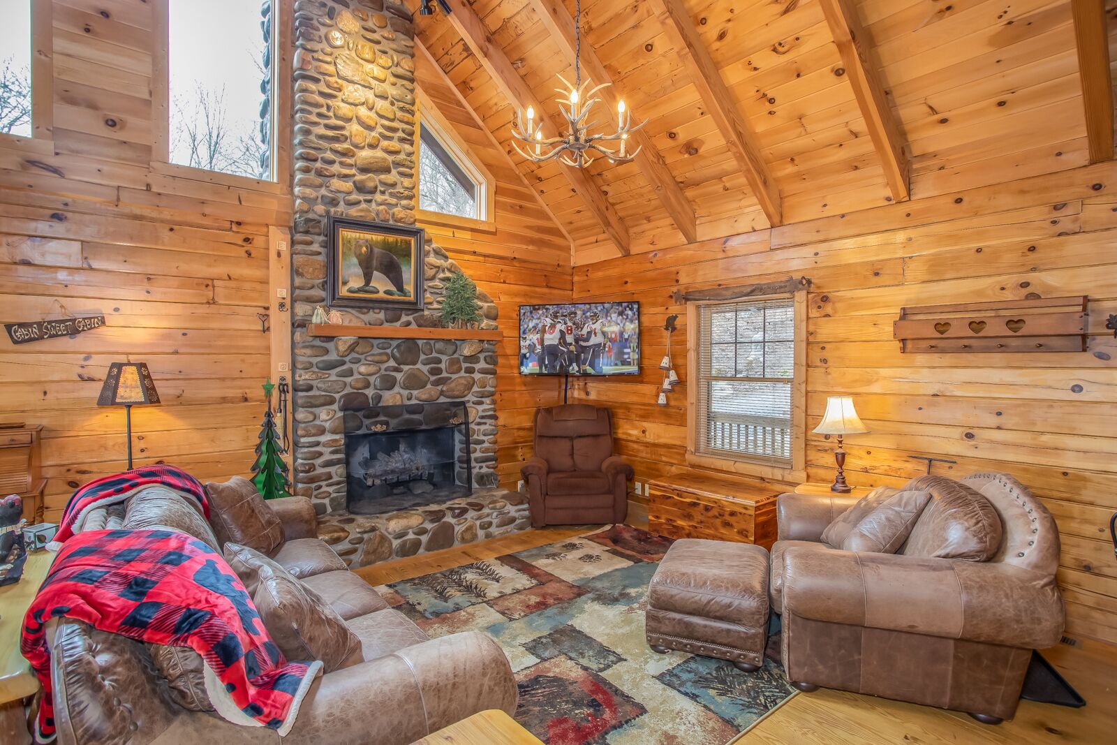 A cozy cabin interior with a stone fireplace, leather sofas, and a large window.