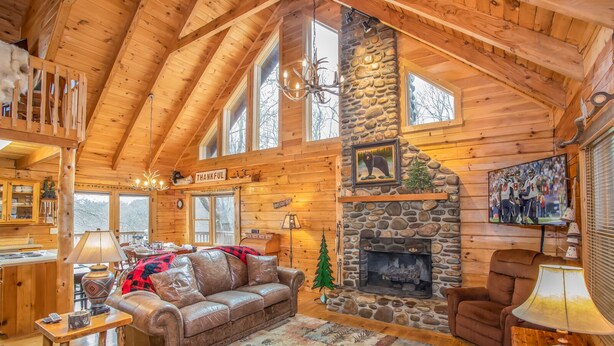 A log cabin interior with a stone fireplace, leather furniture, and a 'THANKFUL' sign.