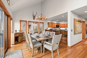 A spacious dining area with a wooden table and chairs, a chandelier with antlers, and a kitchen in the background. - Upscale Mountain Home Near Trails (Boone)