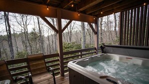 Eine Holzterrasse mit Whirlpool, Holzstühlen und Blick auf einen Wald.