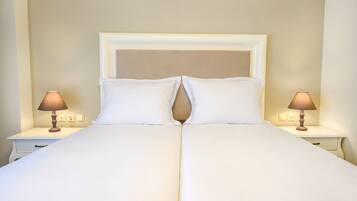 Una cama bien hecha con cabecera blanca, dos lámparas de noche y una mesita de noche blanca con un cajón.