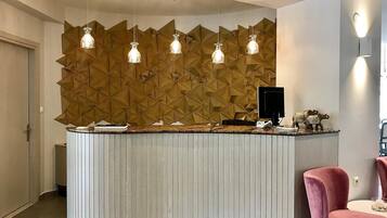 Una recepción con un muro de diseño geométrico, iluminación colgante y un monitor de computadora.