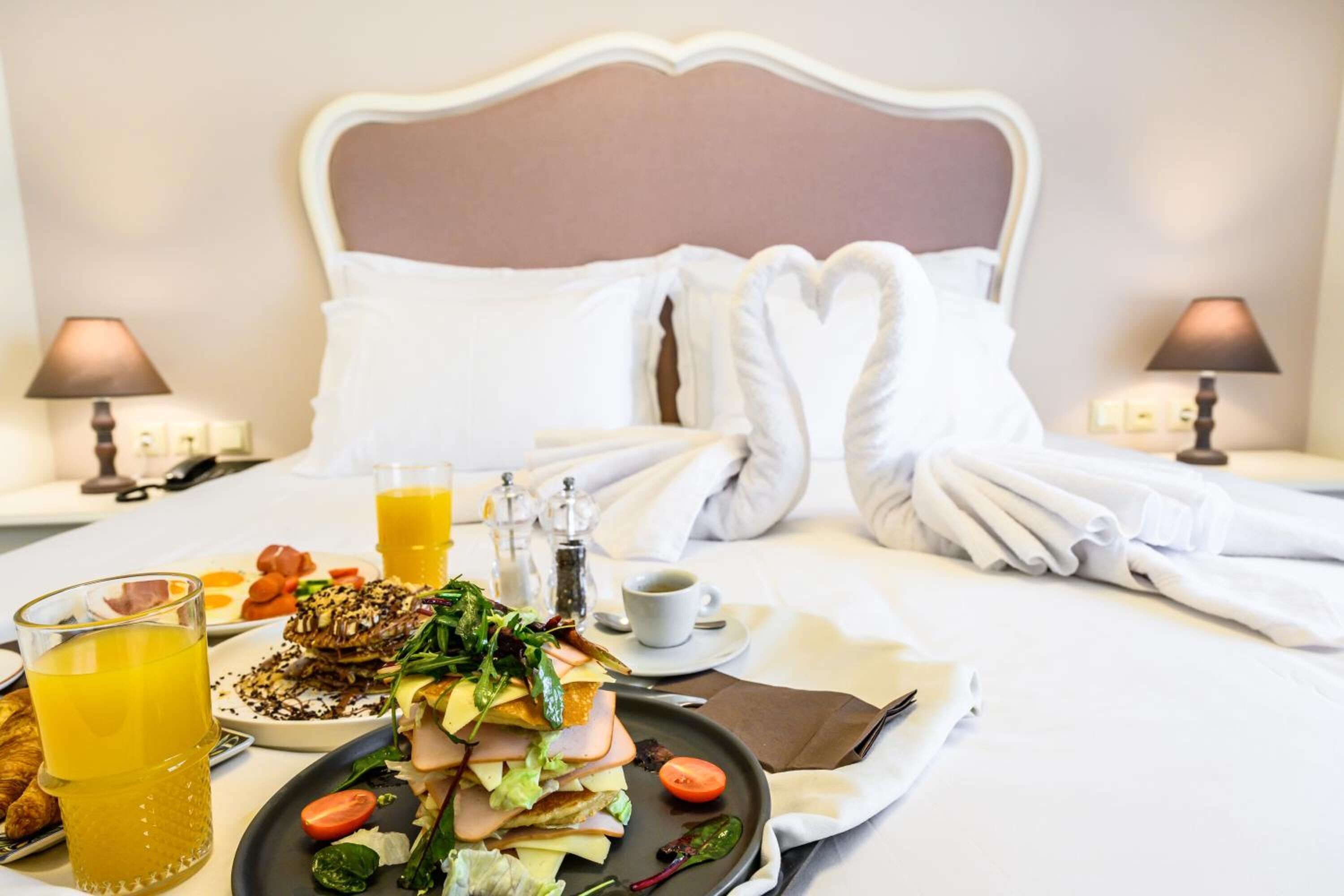 A neatly made bed with white linens and pillows, a breakfast tray with eggs, toast, and a salad, and two lamps on either side of the bed.