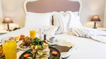 A neatly made bed with white linens and pillows, a breakfast tray with eggs, toast, and a salad, and two lamps on either side of the bed.