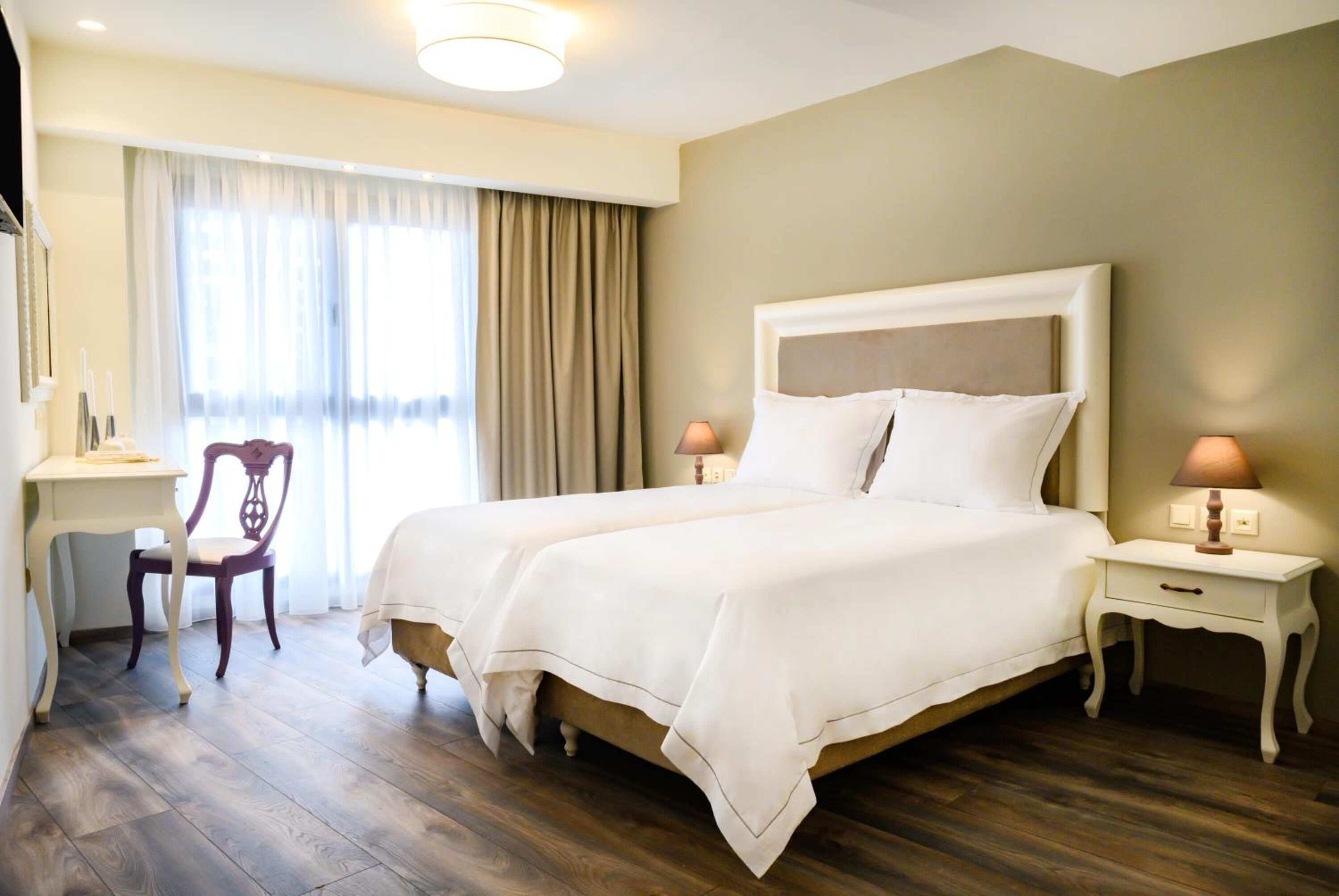 A hotel room with a large bed, two bedside tables, a chair, a desk, and a window with curtains.